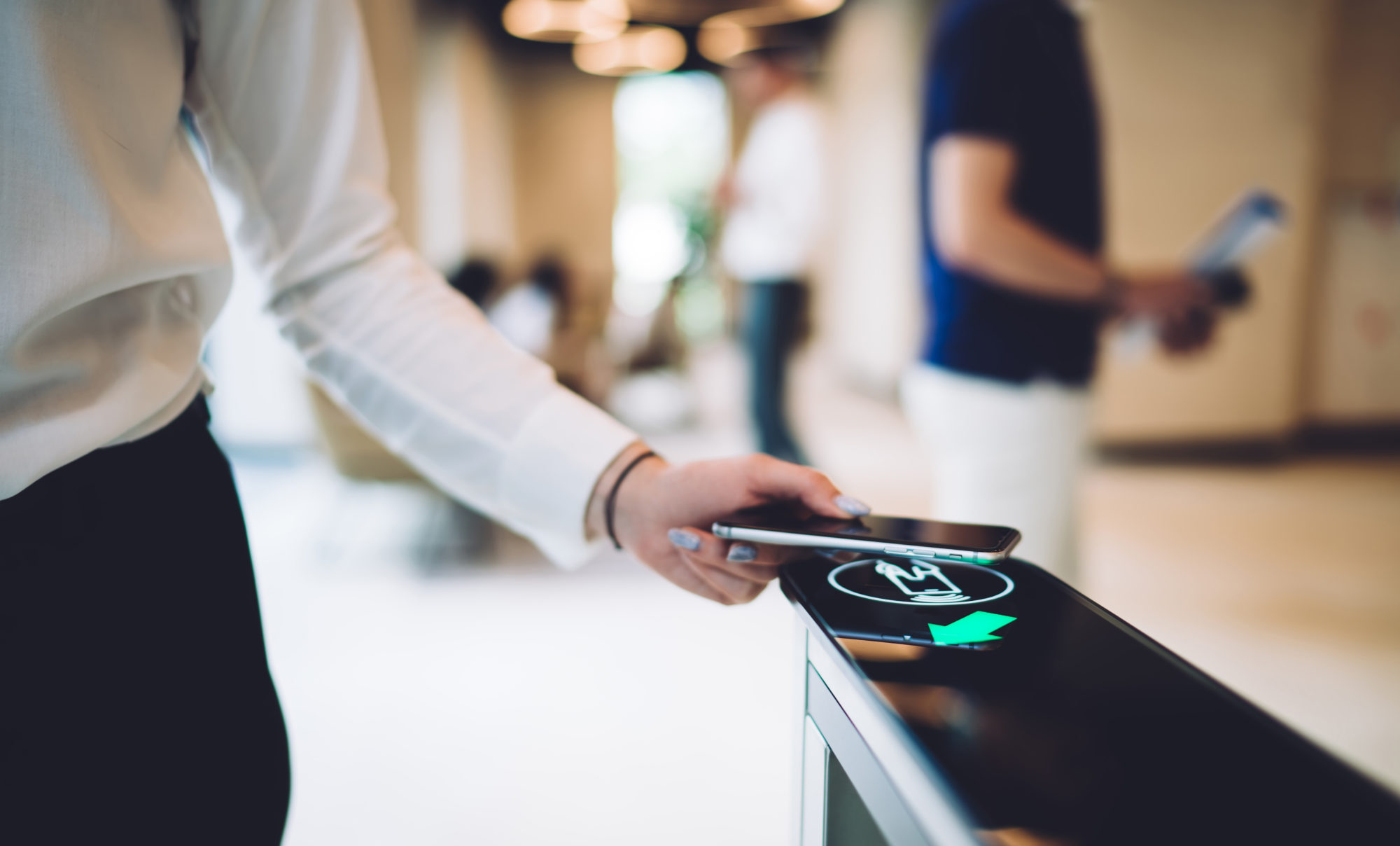 A tenant is seamlessly using smartphone technology to access a security gate in an office setting. The contactless system highlights the ease of tenant-facing technology while, in the blurred background, another person holds documents.