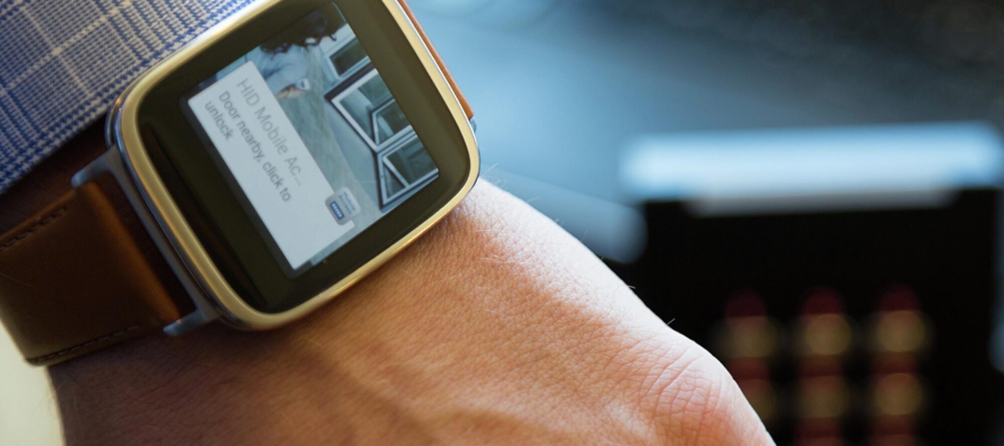 A close-up of a person wearing a smartwatch on their wrist reveals the screen displaying an incoming call notification labeled MID Mobile AC. The watch features a brown leather strap, offering modern tech solutions like mobile credentialing right at your fingertips.