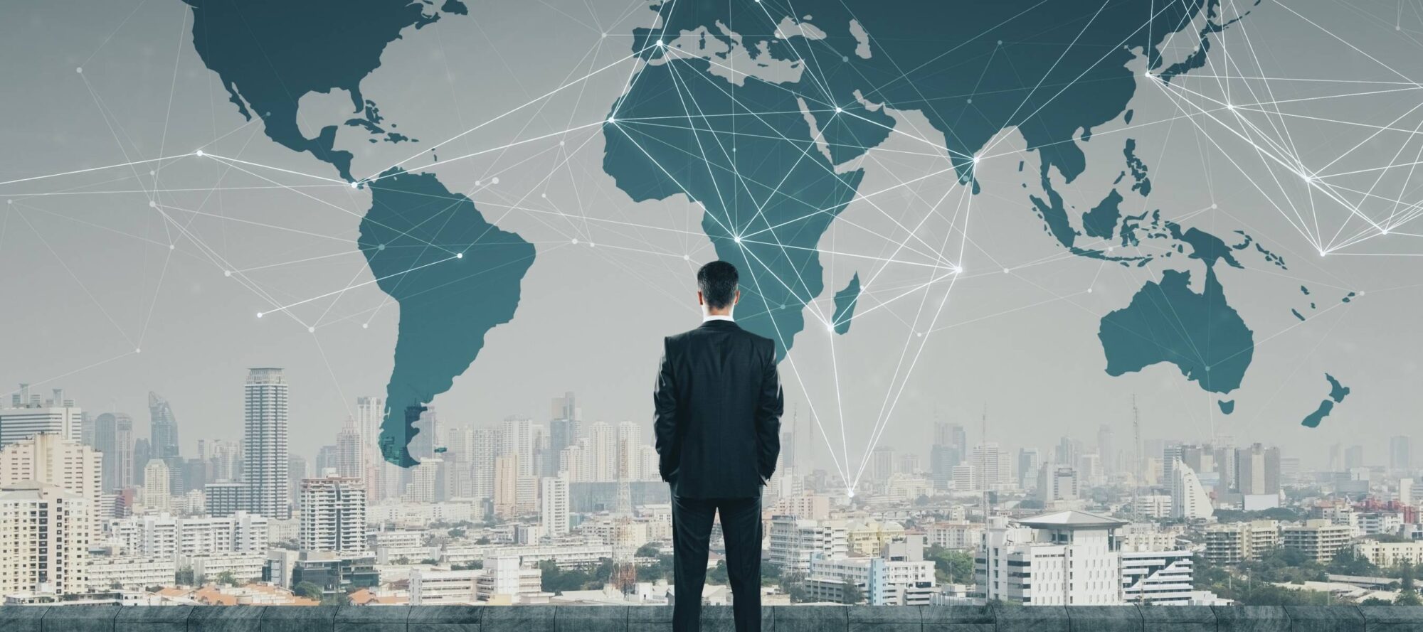 A man in a suit stands facing a city skyline, with a large world map overlayed above, resembling a global dashboard. The interconnected lines on the map highlight international business and communication.