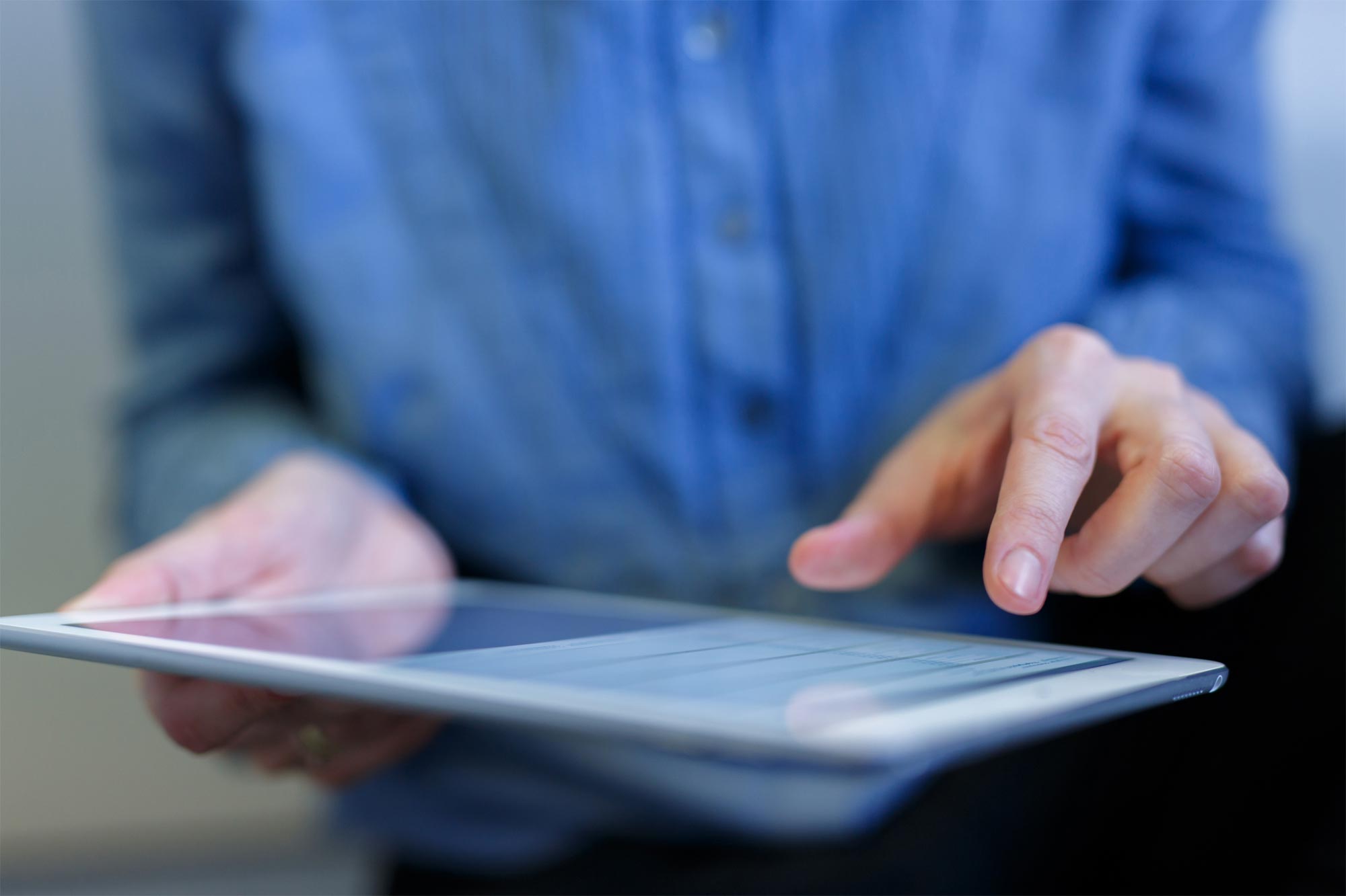 A person wearing a blue shirt is using a tablet, tapping on the screen with their index finger. The focus is on their hands and the device, highlighting how integrator partners enhance interaction with technology.