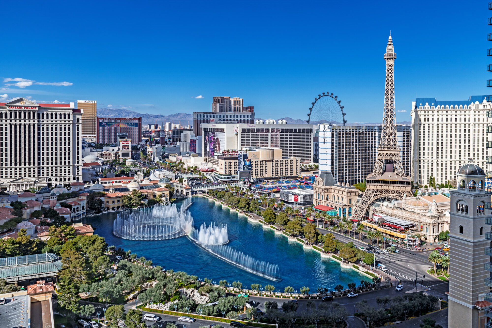 Aerial view of Las Vegas Strip showcasing the Eiffel Tower replica, Bellagio fountains, and various hotels and casinos under a clear blue sky. The High Roller observation wheel is visible in the background as attendees gather for ISC West.