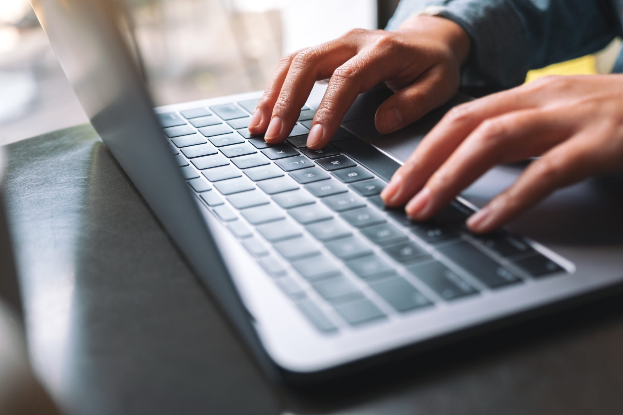 Close-up of hands typing on a laptop keyboard, with sunlight softly illuminating the scene. The laptop is positioned on a dark surface, and the image focuses on the fingers and keys, suggesting an active and focused work environment dedicated to seamless custom webhook configuration.