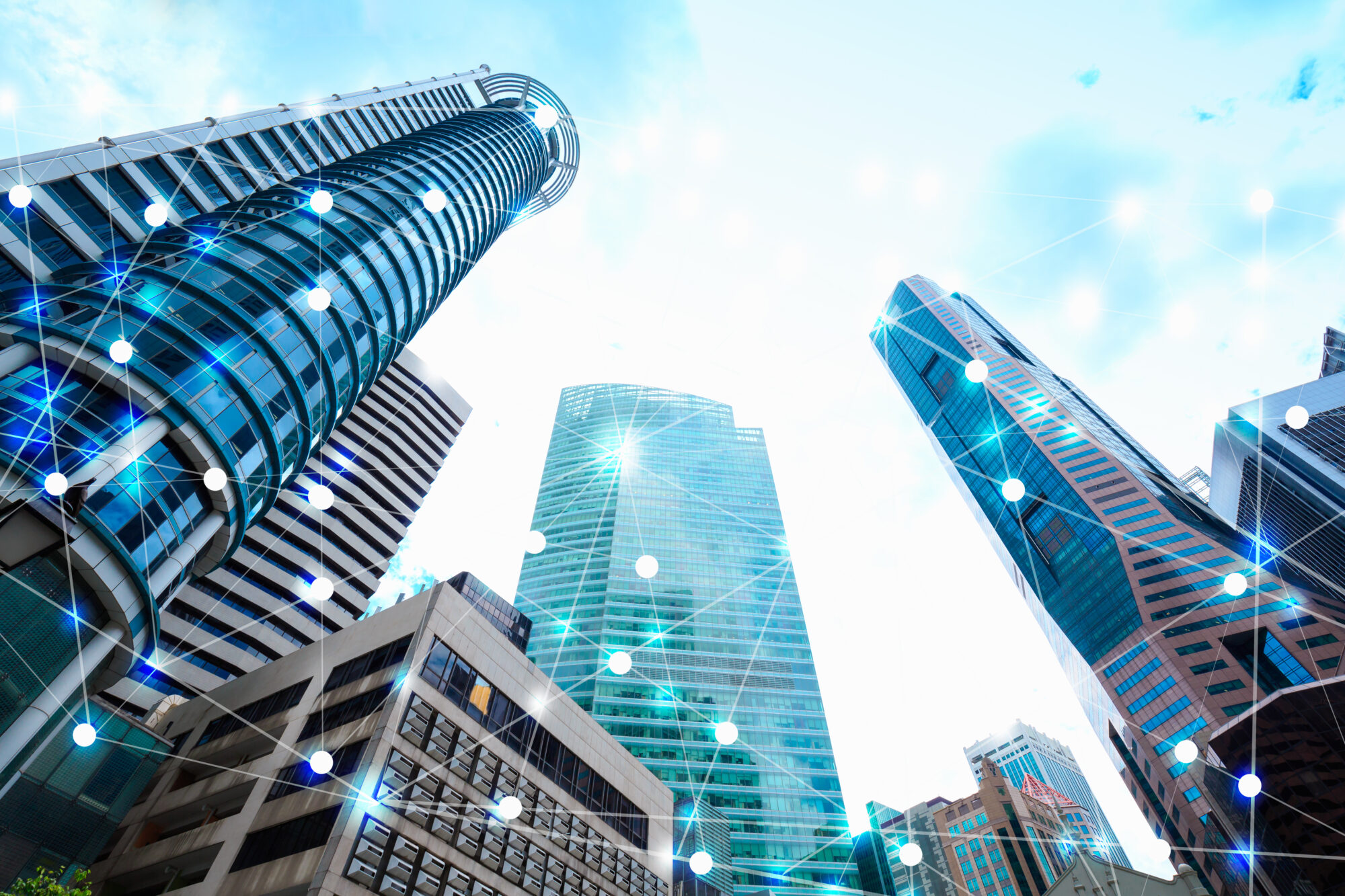 Futuristic skyscrapers against a blue sky, with a digital network overlay of interconnected white dots and lines, symbolizing connectivity and modern technology. The scene evokes seamless over-the-air updates enhancing the smart city's dynamic infrastructure.