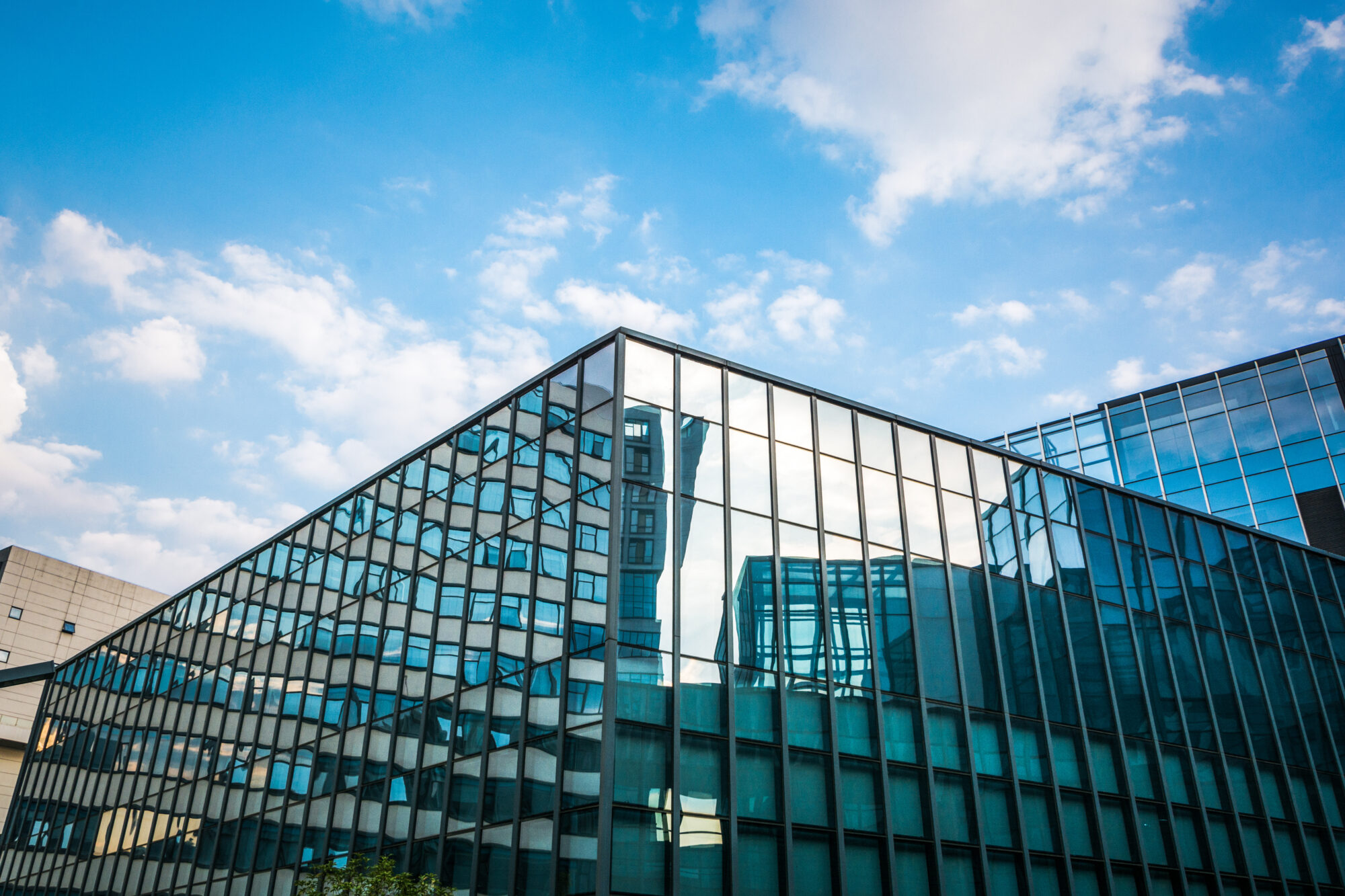 A modern glass building reflecting the blue sky and clouds showcases its geometric lines, creating a striking visual effect. The structure is equipped with smart gas meters, optimizing energy efficiency. Other buildings are visible in the background.