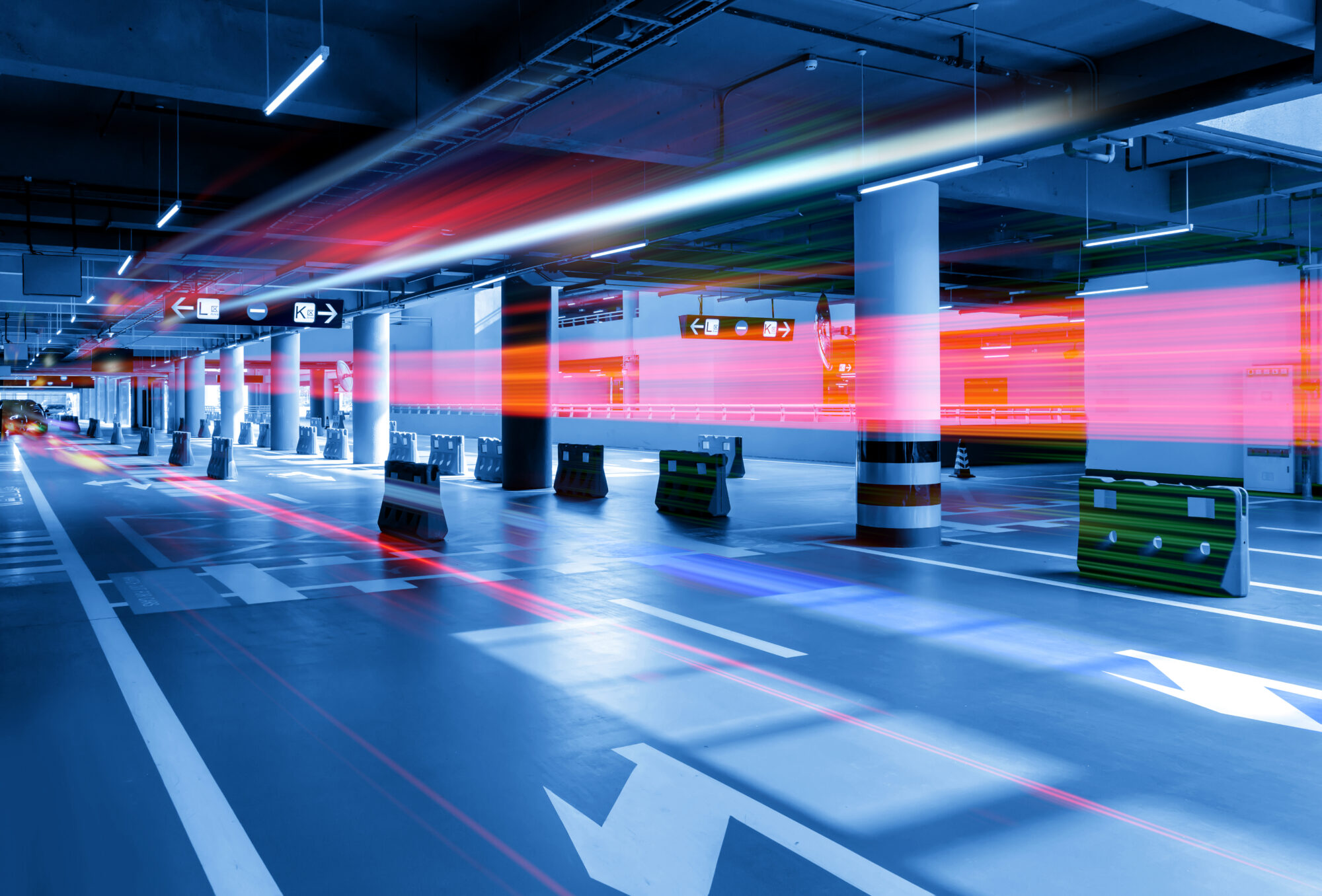 A futuristic underground parking garage with red and blue light streaks creating a motion blur effect. White arrows, clear signs, and sophisticated parking access control systems guide through the space, enhancing its modern and dynamic atmosphere.