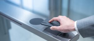 A person in a suit uses mobile credentials on a smartphone to scan at an electronic access control system, likely for entry. The image focuses on the hand holding the phone against a sleek, metallic scanner.