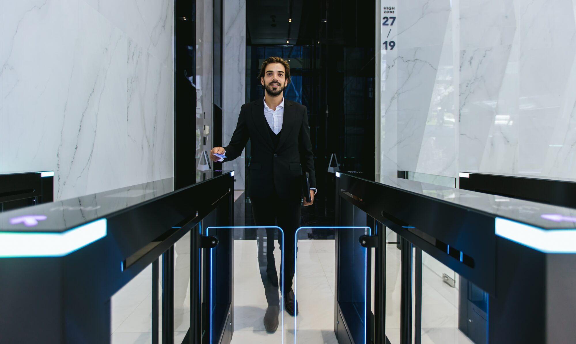 A man in a suit confidently walks through a modern security turnstile, exemplifying the evolution of access control in an office building lobby. The glass and marble walls create a sleek, professional atmosphere.